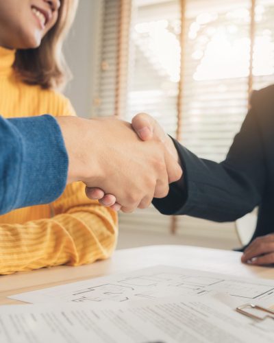 Happy young Asian couple and realtor agent. Cheerful young man s Happy young Asian couple and realtor agent. Cheerful young man signing some documents and handshaking with broker while sitting at desk. Signing good condition contract.